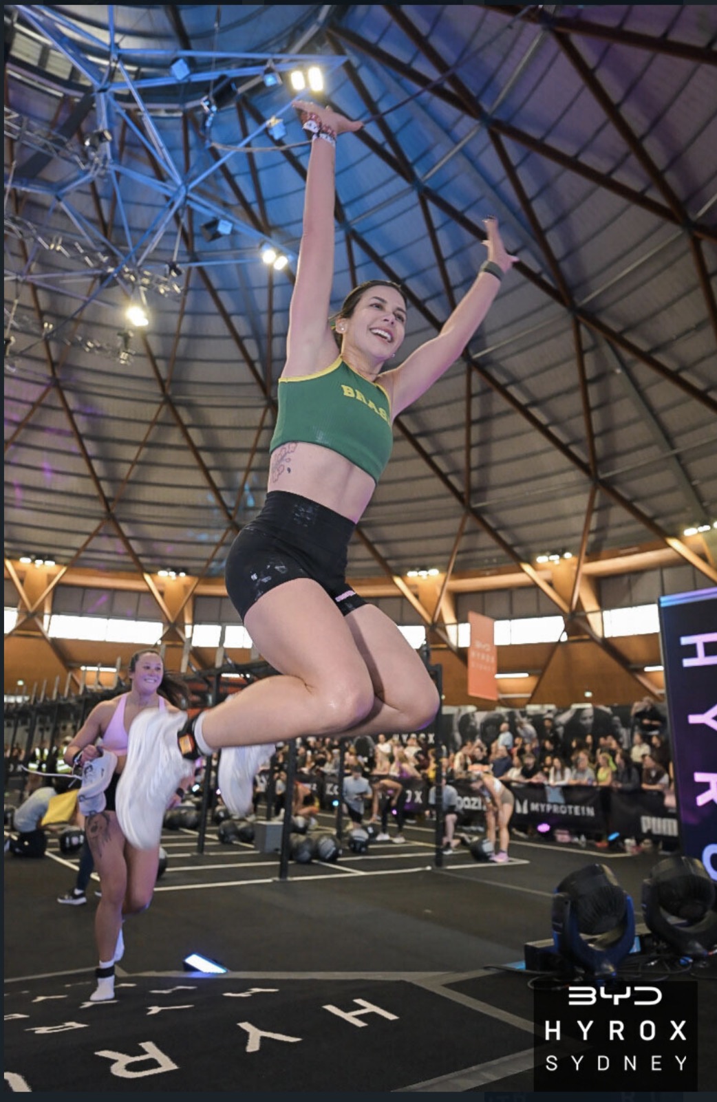 Mari Walks leaping with arms raised in celebration at HYROX Sydney inside a packed event arena